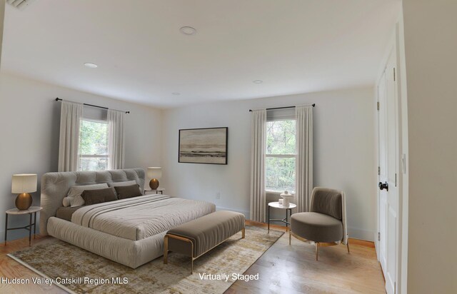 bedroom with an AC wall unit, light hardwood / wood-style flooring, and multiple closets