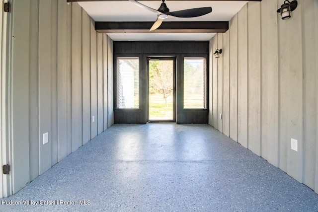 unfurnished room featuring a ceiling fan, wood walls, and speckled floor
