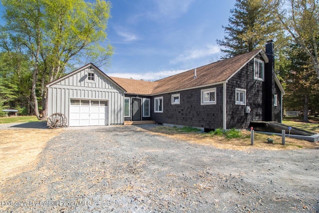 single story home featuring a chimney, a shingled roof, board and batten siding, an attached garage, and driveway