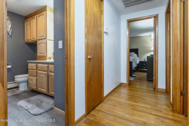 hall featuring a baseboard radiator, baseboards, light wood-style floors, and visible vents