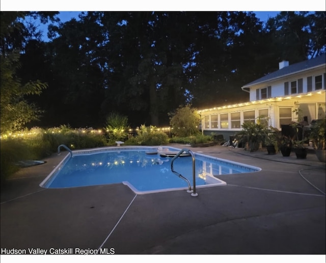pool at night featuring a sunroom, an outdoor pool, and a patio
