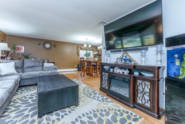 living area with a baseboard radiator, an inviting chandelier, wood finished floors, and visible vents