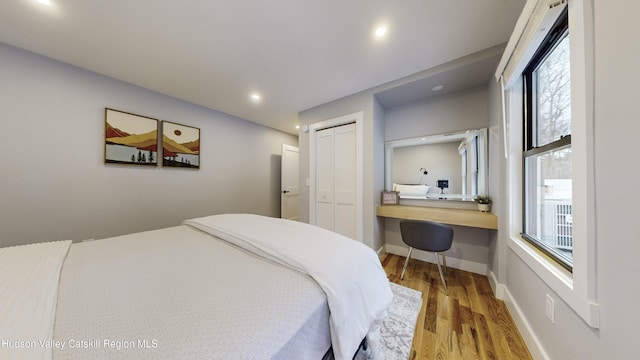 bedroom with wood-type flooring, multiple windows, a closet, and built in desk