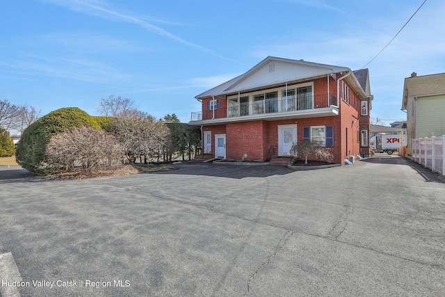 view of front of home featuring a balcony, fence, and brick siding