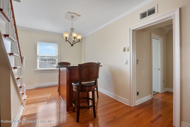dining room with ornamental molding, light wood finished floors, visible vents, a baseboard radiator, and a notable chandelier