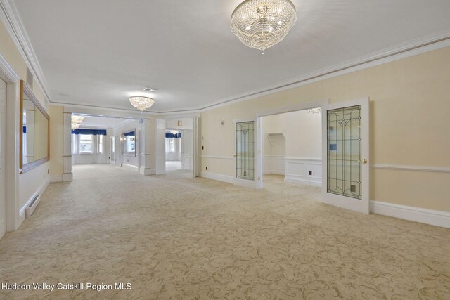 carpeted empty room with visible vents, a decorative wall, crown molding, and a notable chandelier