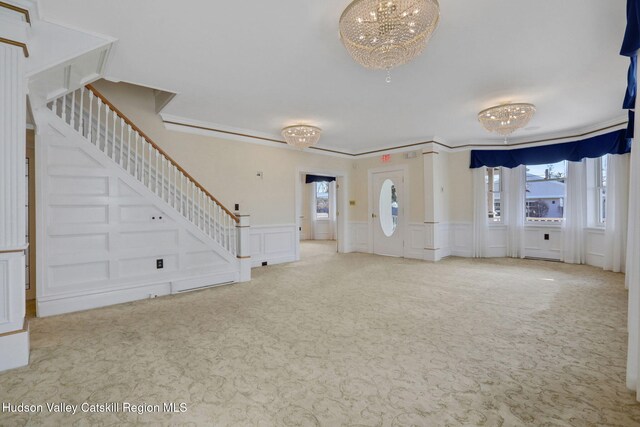 unfurnished living room featuring carpet flooring, plenty of natural light, a chandelier, and stairs