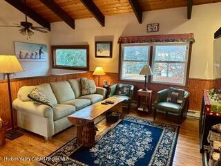 212 S St, Windham, NY 12496 - living room with wood ceiling with exposed beams, a wainscoted wall, ceiling fan, wood finished floors, and wood walls
