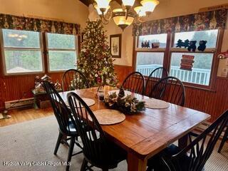 212 S St, Windham, NY 12496 - carpeted dining area featuring wood walls, a chandelier, baseboard heating, and wood finished floors