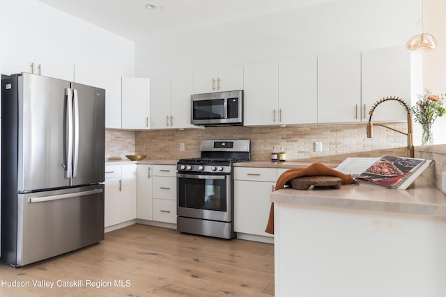 kitchen featuring appliances with stainless steel finishes, decorative backsplash, white cabinets, hanging light fixtures, and light hardwood / wood-style flooring