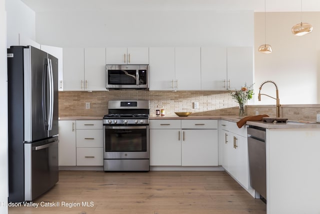 kitchen with hanging light fixtures, backsplash, stainless steel appliances, and white cabinetry