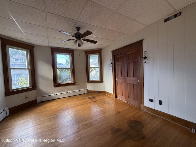 spare room with a paneled ceiling, light hardwood / wood-style flooring, and a baseboard heating unit