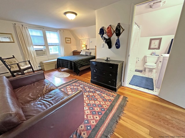 bedroom with hardwood / wood-style flooring, cooling unit, ensuite bathroom, and vaulted ceiling