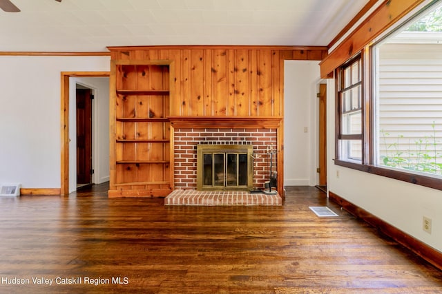 unfurnished living room featuring crown molding, wooden walls, dark hardwood / wood-style floors, built in shelves, and a fireplace