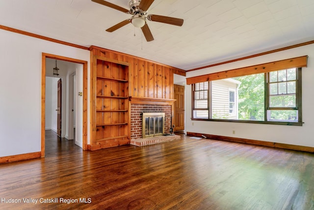 unfurnished living room with built in shelves, dark hardwood / wood-style flooring, a brick fireplace, and ornamental molding