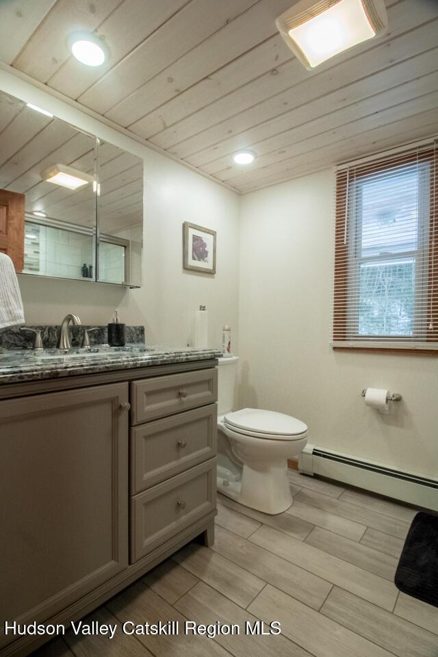 50 Tempaloni Rd, Ellenville, NY 12428 - full bath featuring wood ceiling, toilet, vanity, wood finished floors, and baseboard heating