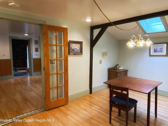 dining area with light hardwood / wood-style flooring, a notable chandelier, and vaulted ceiling with skylight