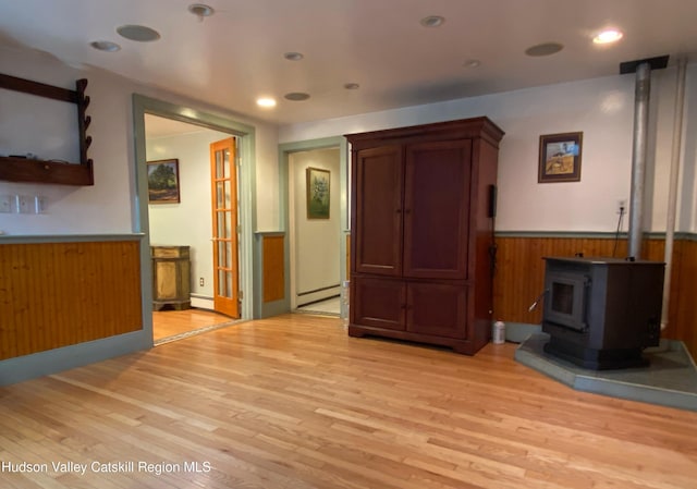 unfurnished living room with light wood-type flooring, a wood stove, and baseboard heating