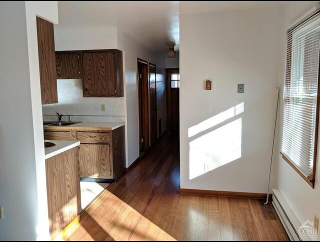kitchen with a baseboard heating unit, light countertops, a sink, dark wood-style flooring, and baseboards