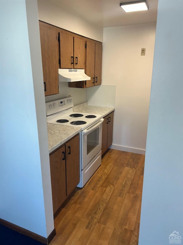 kitchen with under cabinet range hood, electric range, wood finished floors, light countertops, and baseboards
