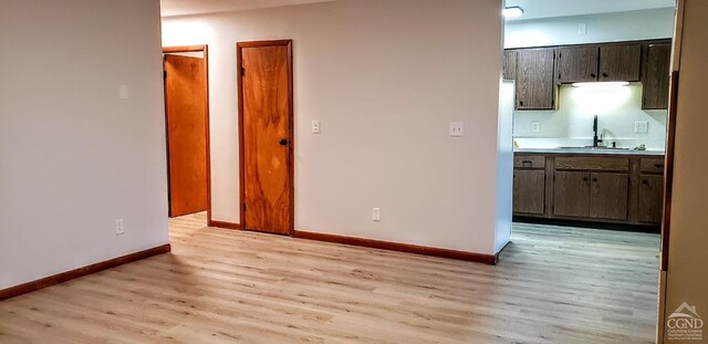 unfurnished living room featuring light wood finished floors, baseboards, and a sink