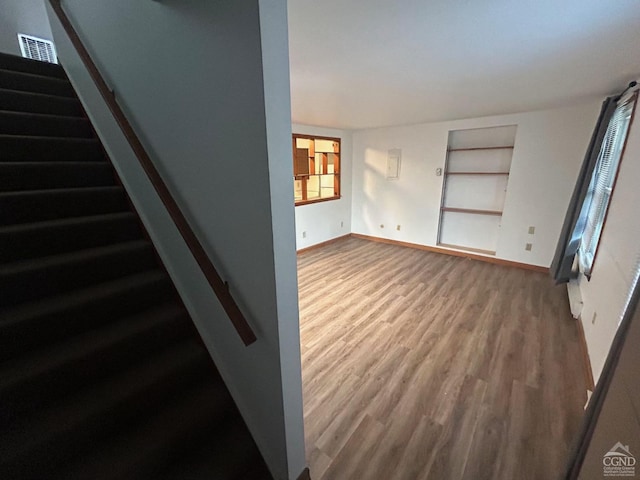 unfurnished living room featuring wood finished floors, stairway, baseboards, and built in shelves
