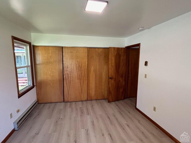unfurnished bedroom featuring baseboard heating, light wood-style floors, a closet, and baseboards