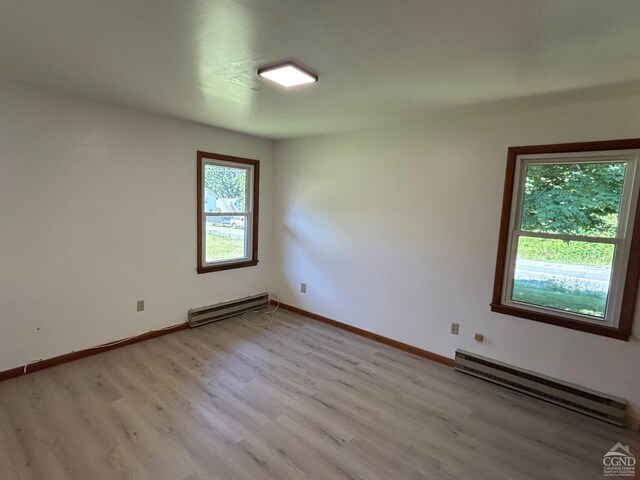 empty room featuring baseboard heating, light wood finished floors, and baseboards