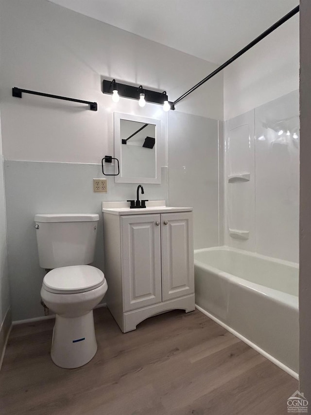 bathroom featuring wood finished floors, toilet, vanity, bathing tub / shower combination, and baseboards