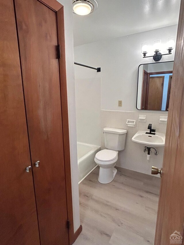 bathroom with wood finished floors, a sink, toilet, tile walls, and wainscoting