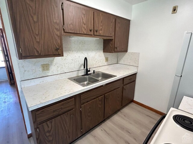 kitchen with a sink, light wood-style floors, white appliances, light countertops, and backsplash