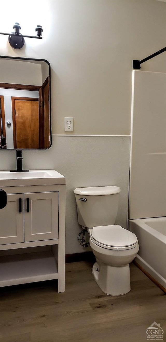 bathroom with wood finished floors, toilet, vanity, and  shower combination