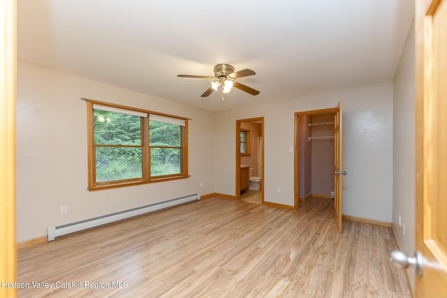 unfurnished bedroom featuring ensuite bath, a spacious closet, baseboard heating, light hardwood / wood-style floors, and a closet