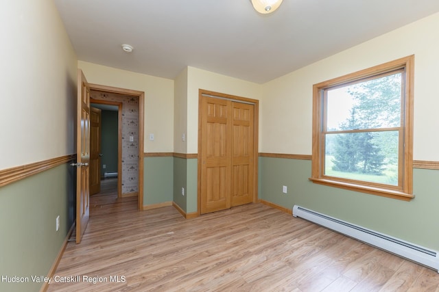 unfurnished bedroom featuring light wood-type flooring, a closet, and a baseboard heating unit