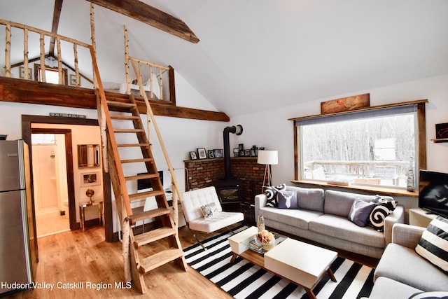 living room featuring light wood-type flooring, vaulted ceiling with beams, and a wood stove