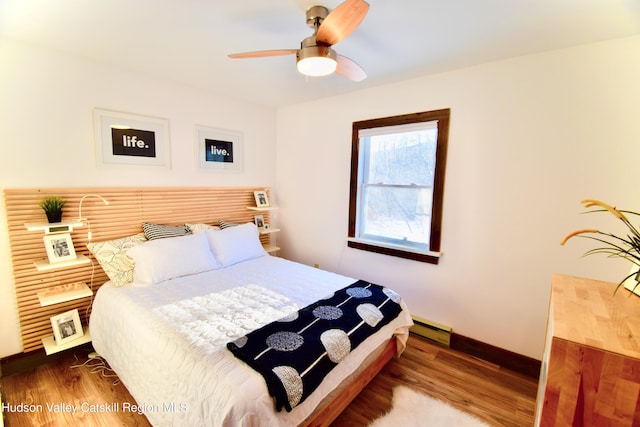 bedroom with hardwood / wood-style flooring, ceiling fan, and a baseboard heating unit