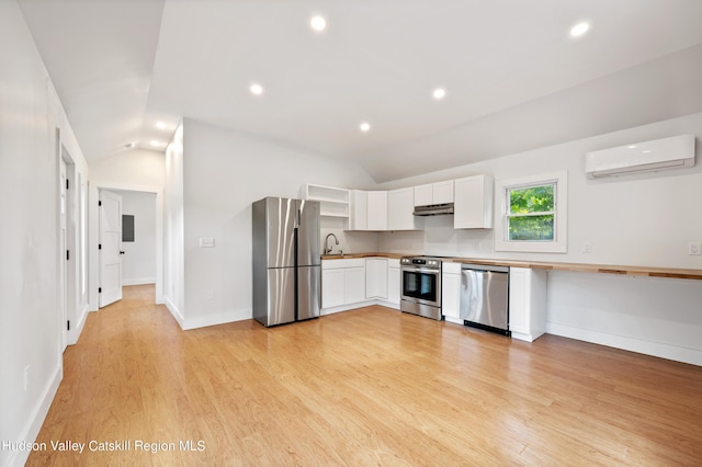 kitchen featuring stainless steel appliances, lofted ceiling, white cabinets, and a wall unit AC