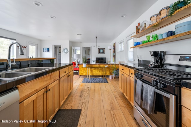 kitchen with dishwasher, sink, hanging light fixtures, stainless steel gas range, and light wood-type flooring