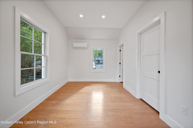 empty room with a wealth of natural light, light hardwood / wood-style flooring, and an AC wall unit