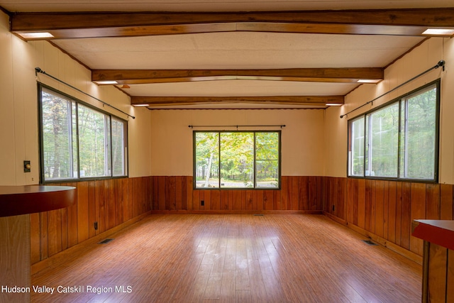 spare room with wood walls, beam ceiling, and light wood-type flooring