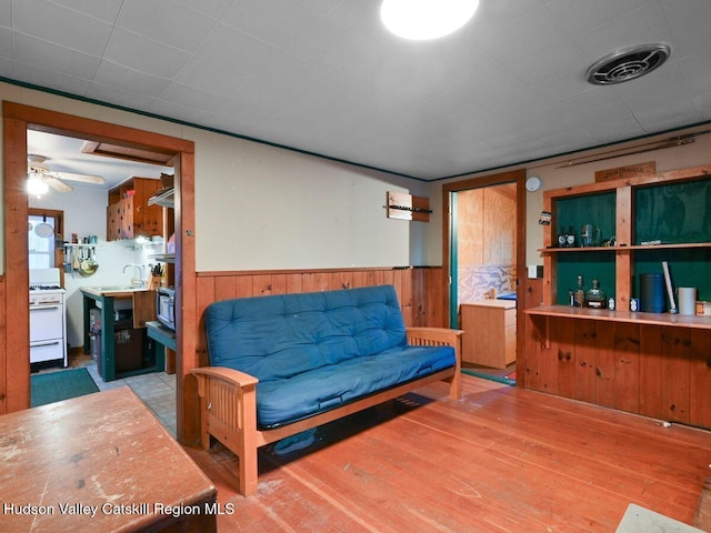 living room featuring hardwood / wood-style flooring, ceiling fan, wooden walls, and sink