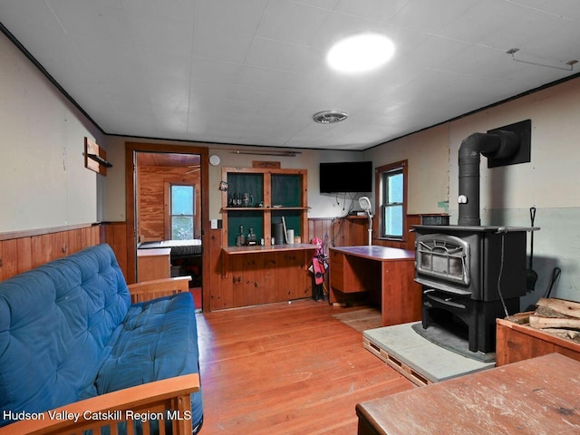 living room with light hardwood / wood-style floors, a wood stove, and wood walls