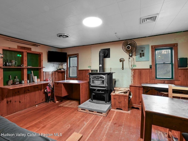 kitchen with wood-type flooring, electric panel, a wood stove, and wooden walls