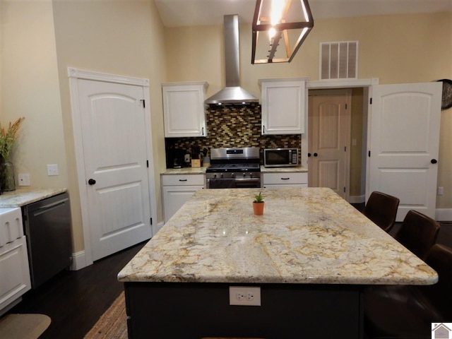 kitchen with stainless steel appliances, white cabinets, wall chimney range hood, a kitchen island, and tasteful backsplash