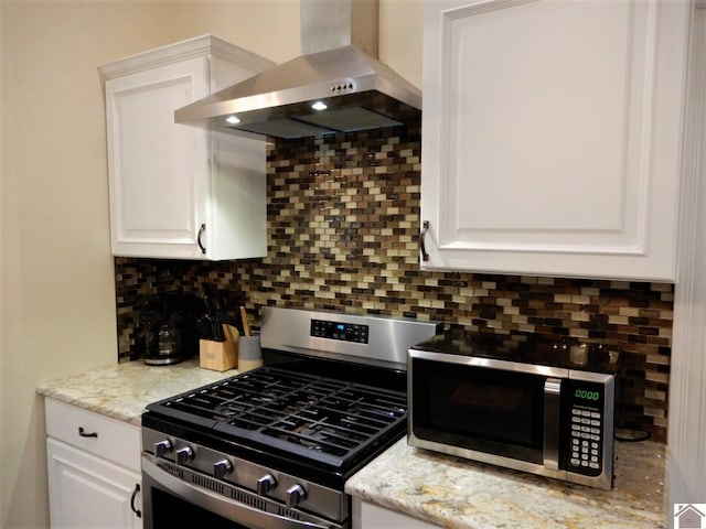 kitchen featuring white cabinets, backsplash, stainless steel appliances, light stone countertops, and wall chimney range hood