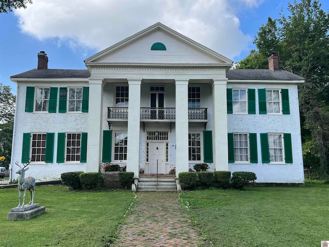 greek revival inspired property with a front lawn and a balcony