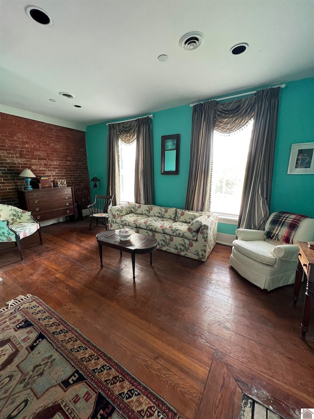 living room with brick wall, dark wood-type flooring, and a wealth of natural light