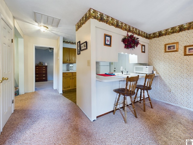 kitchen with kitchen peninsula, ceiling fan, white appliances, a kitchen bar, and carpet