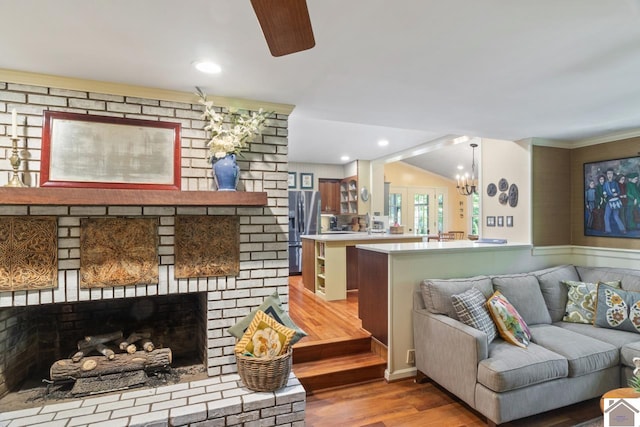 living room with a fireplace, ceiling fan with notable chandelier, lofted ceiling, brick wall, and wood-type flooring