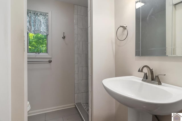 bathroom with sink, toilet, a tile shower, and tile patterned flooring